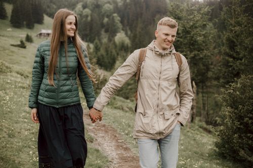 Free A couple enjoying a walk through a lush, green countryside, holding hands and smiling. Stock Photo