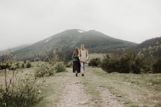 A couple enjoying a peaceful walk through lush green mountains on a cloudy day.