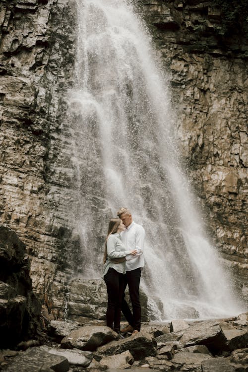 Photo of a Couple Standing Beside a Waterfall