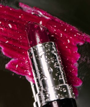 Close-up of a lipstick with reflective water droplets, highlighting vibrant cosmetics.