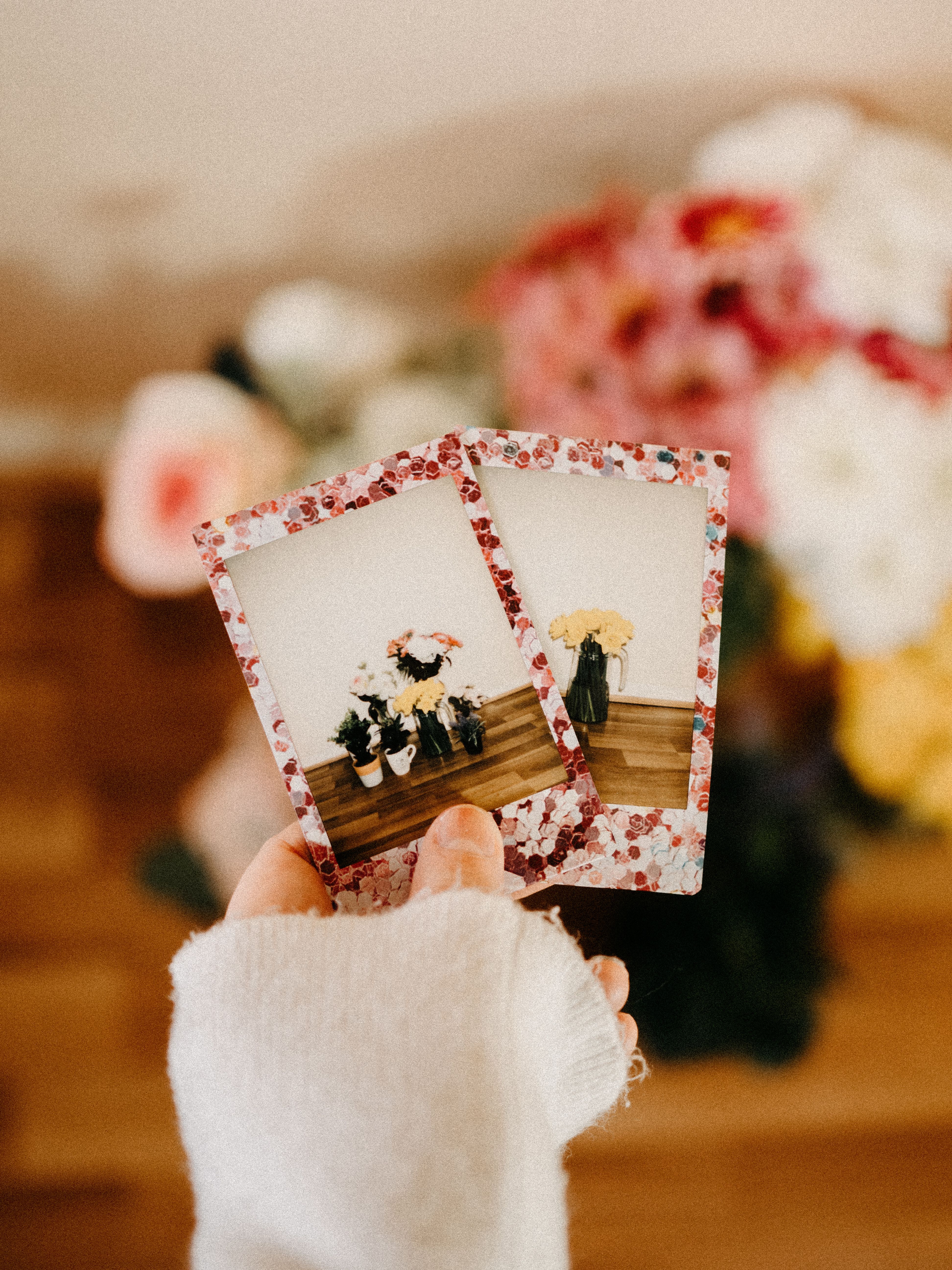 A person holding floral-themed polaroids with a blurred bouquet in the background.