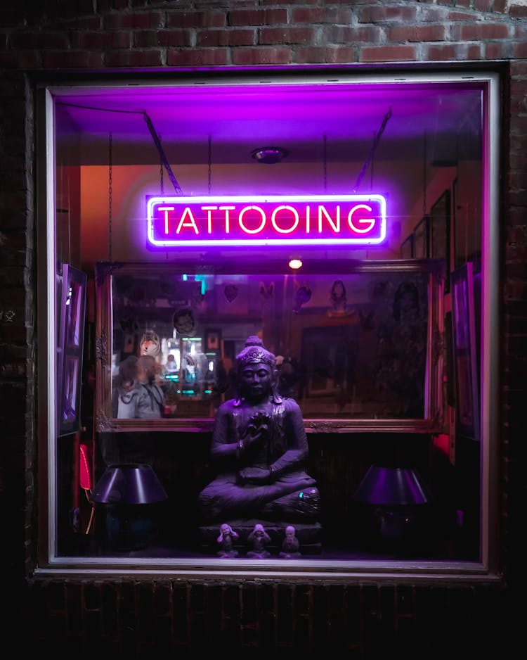 Neon Sign And Buddha Statue In Tattoo Parlor Window