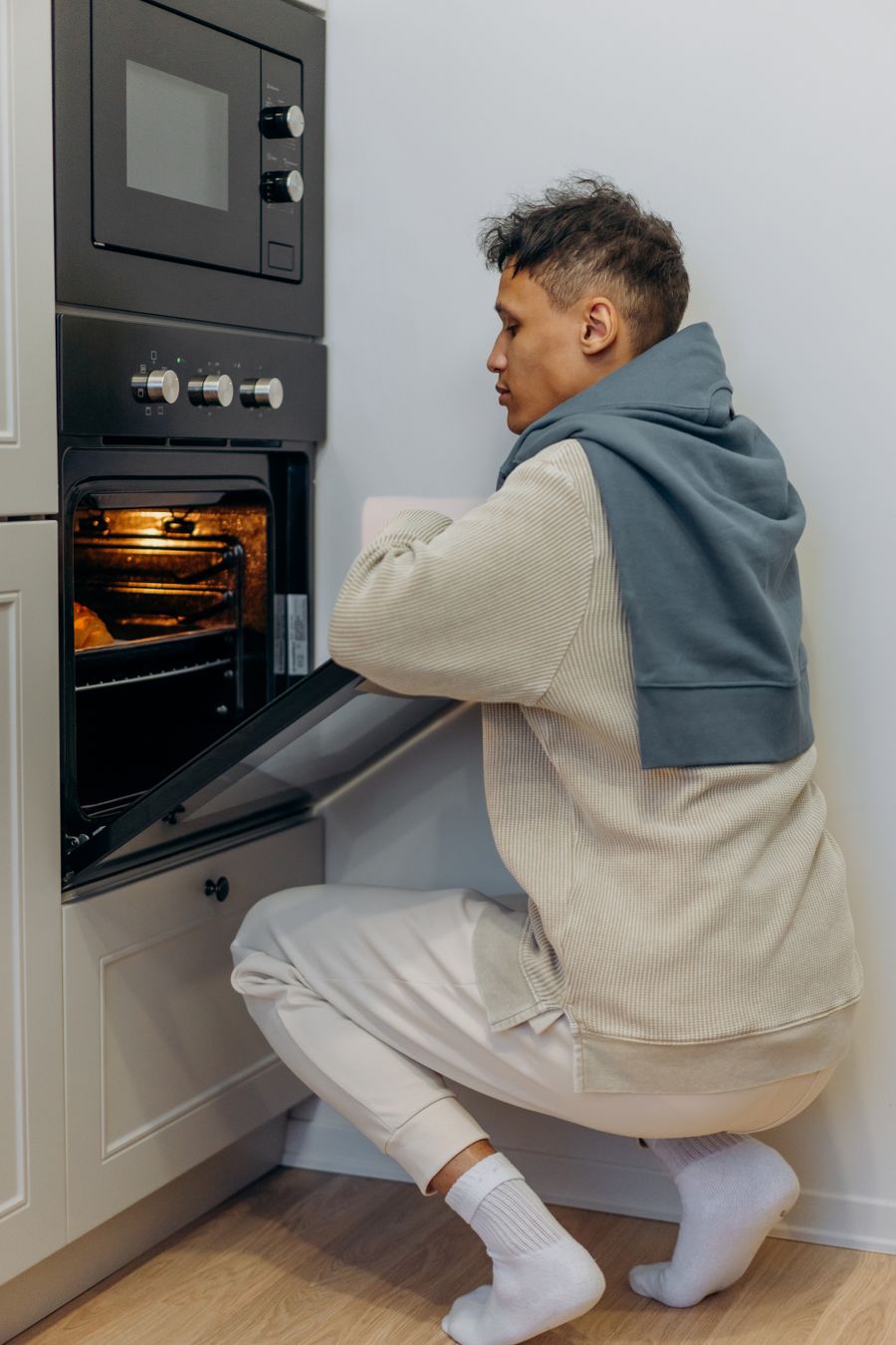 A person crouching to look through a wall oven door