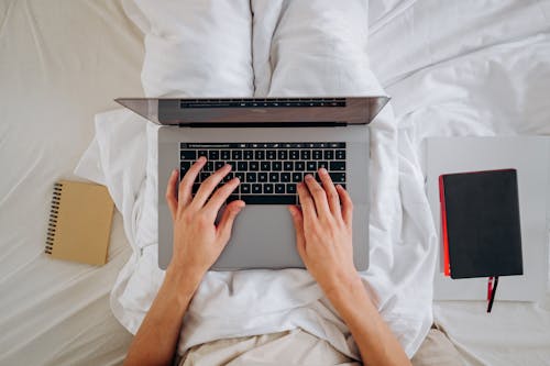 Person Sitting on the Bed Using a Laptop 