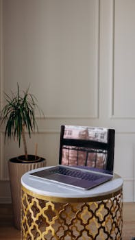 A sleek laptop on a chic gold table beside a home plant in a stylish indoor setting.