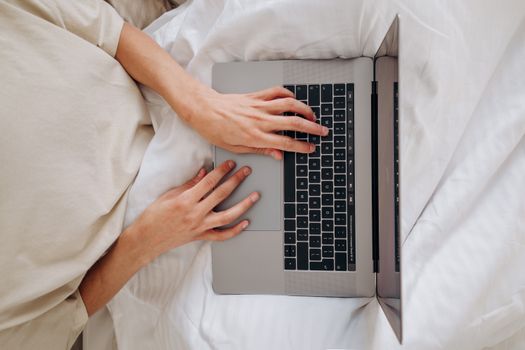 Top view of a person typing on a laptop, seated on a bed with a white blanket.