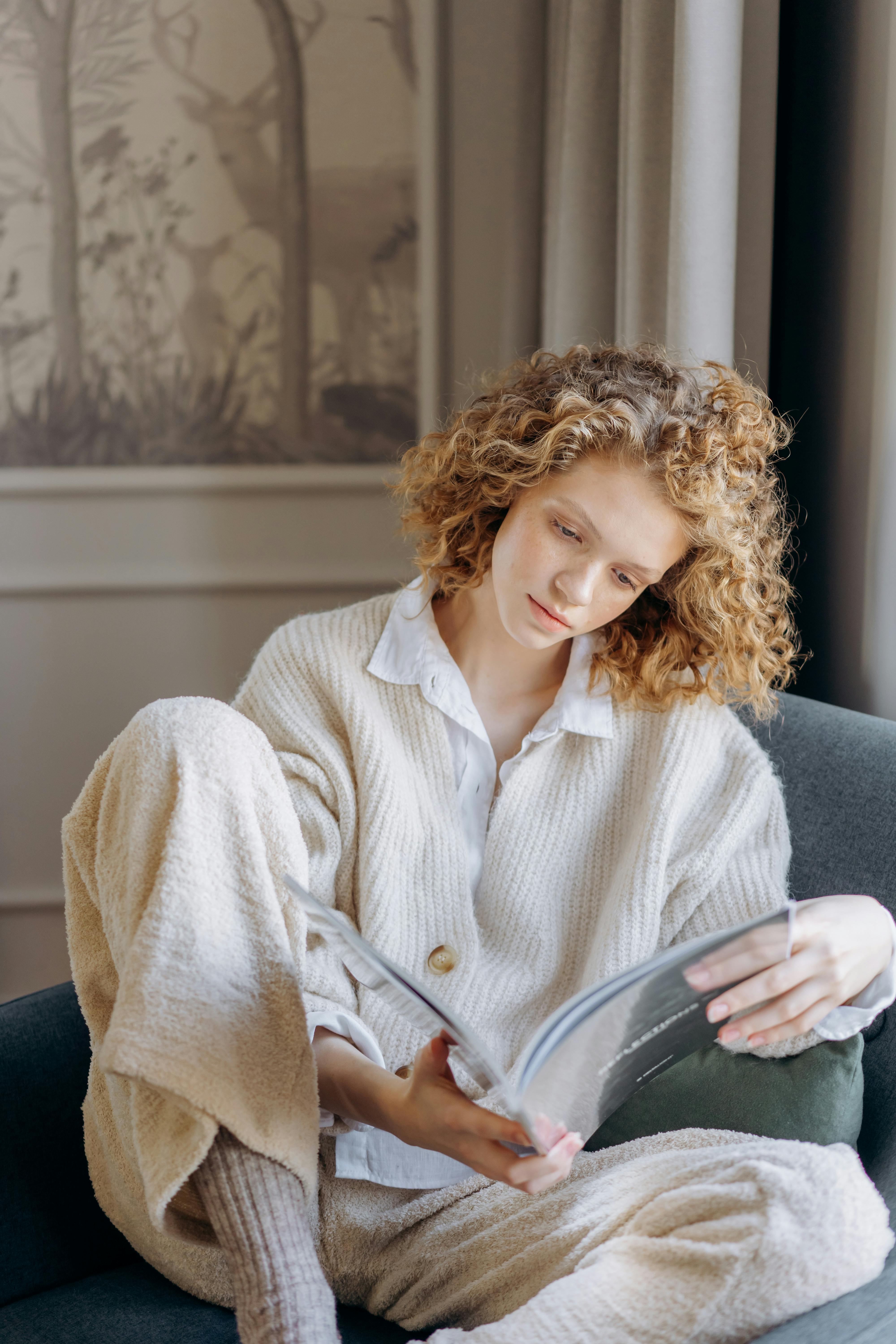 A woman enjoys a peaceful moment reading on a cozy armchair indoors.