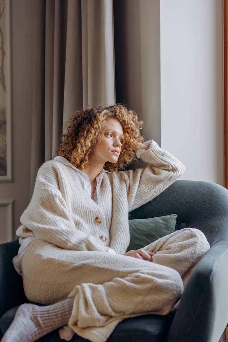 Woman Wearing Knitted Sweater And Pants With Socks Sitting On Couch