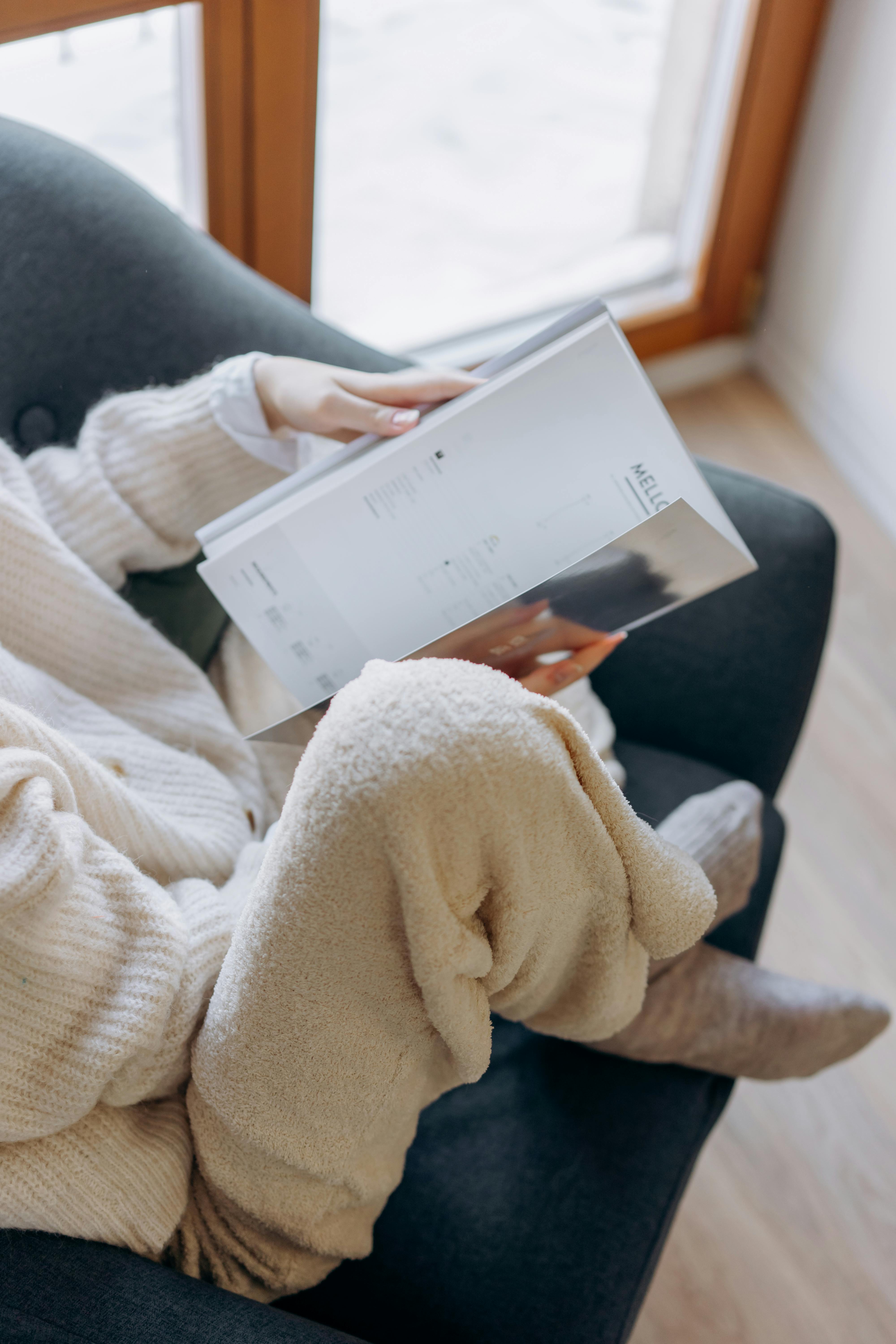 Free Woman enjoying a relaxing moment, reading an open book in cozy indoor setting. Stock Photo