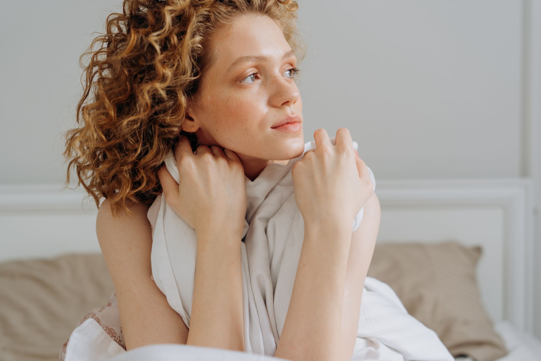 person waking up refreshed in soft morning light, stretching peacefully in bed with white linens