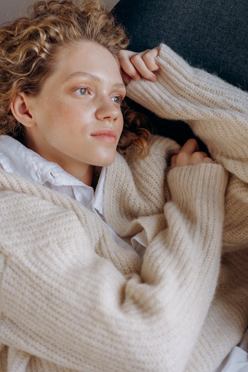 Free Woman in Beige Sweater Lying on Gray Textile Stock Photo
