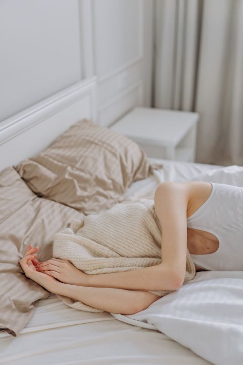 Free Woman lying in bed with a blanket covering her face in a bright, cozy bedroom. Stock Photo