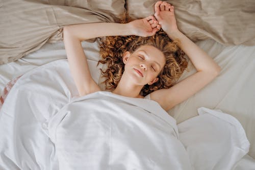 Free Woman With Curly Hair Lying Down on Bed With White Blanket Stock Photo