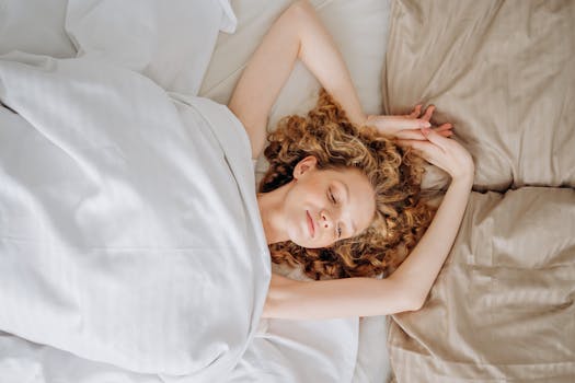 A woman with curly hair stretches in bed, enjoying a cozy morning with soft linens.