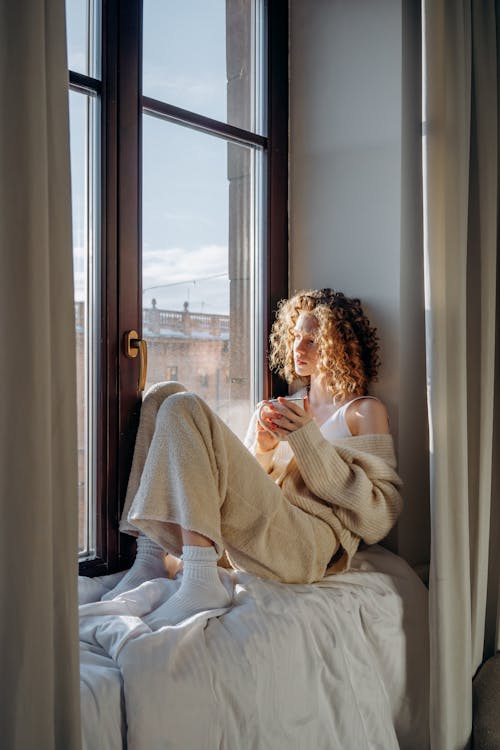 Woman in White Sweater Sitting By the Glass Window