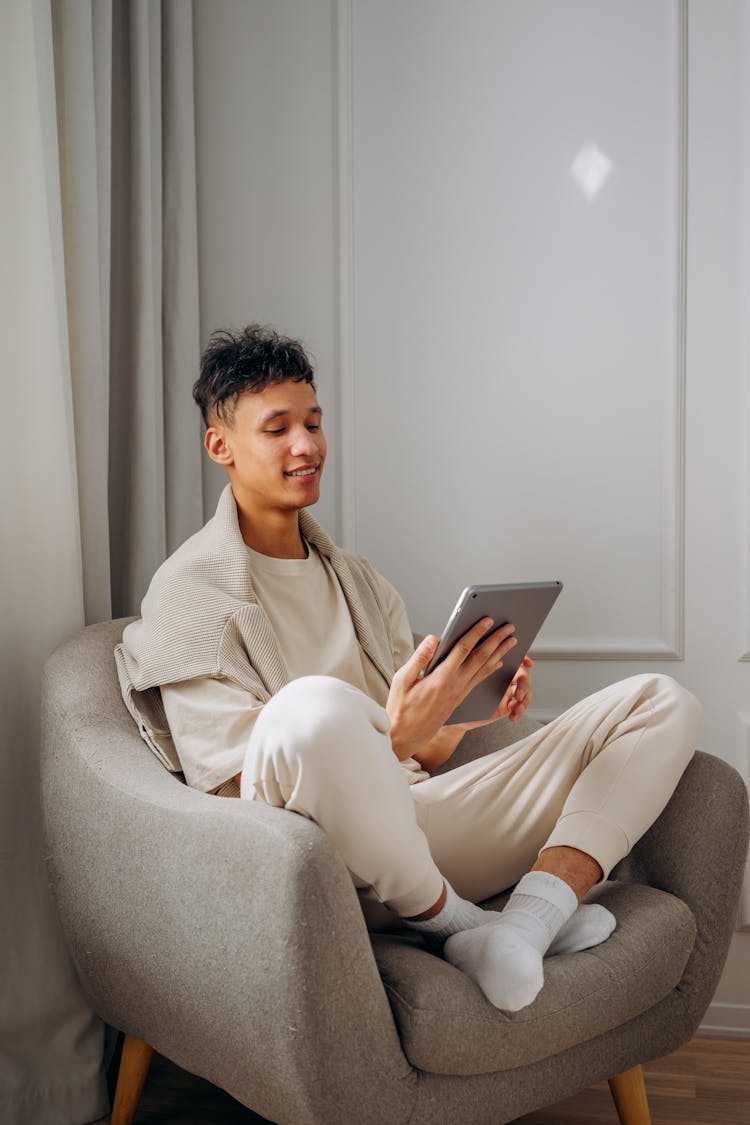 Man Sitting On Sofa Chair While Holding A Tablet