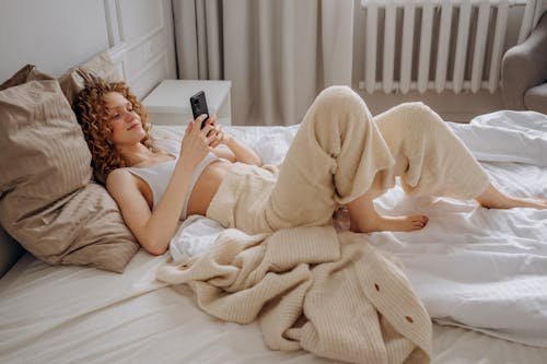 Woman in White Crop Top Lying Down on Bed Using Smartphone