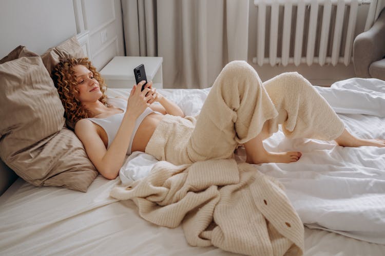 Woman In White Crop Top Lying Down On Bed Using Smartphone