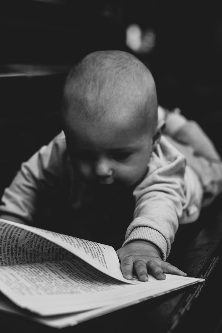 Grayscale Photo Of Baby Turning The Book Page 