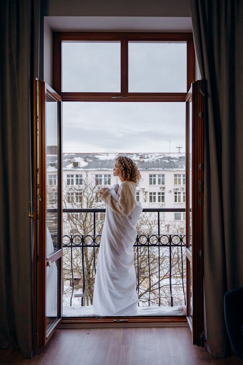 Free Woman Covered with White Blanket while Standing on the Balcony  Stock Photo