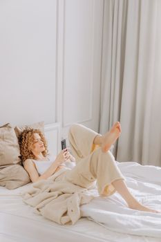 A woman relaxes on a comfortable bed while using her smartphone, enjoying a peaceful indoor moment.