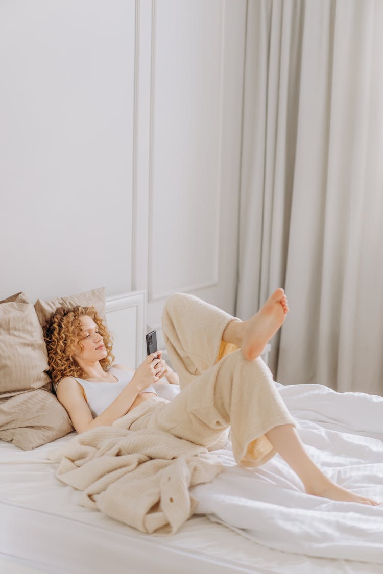 Woman Lying On Bed While Using A Cellphone