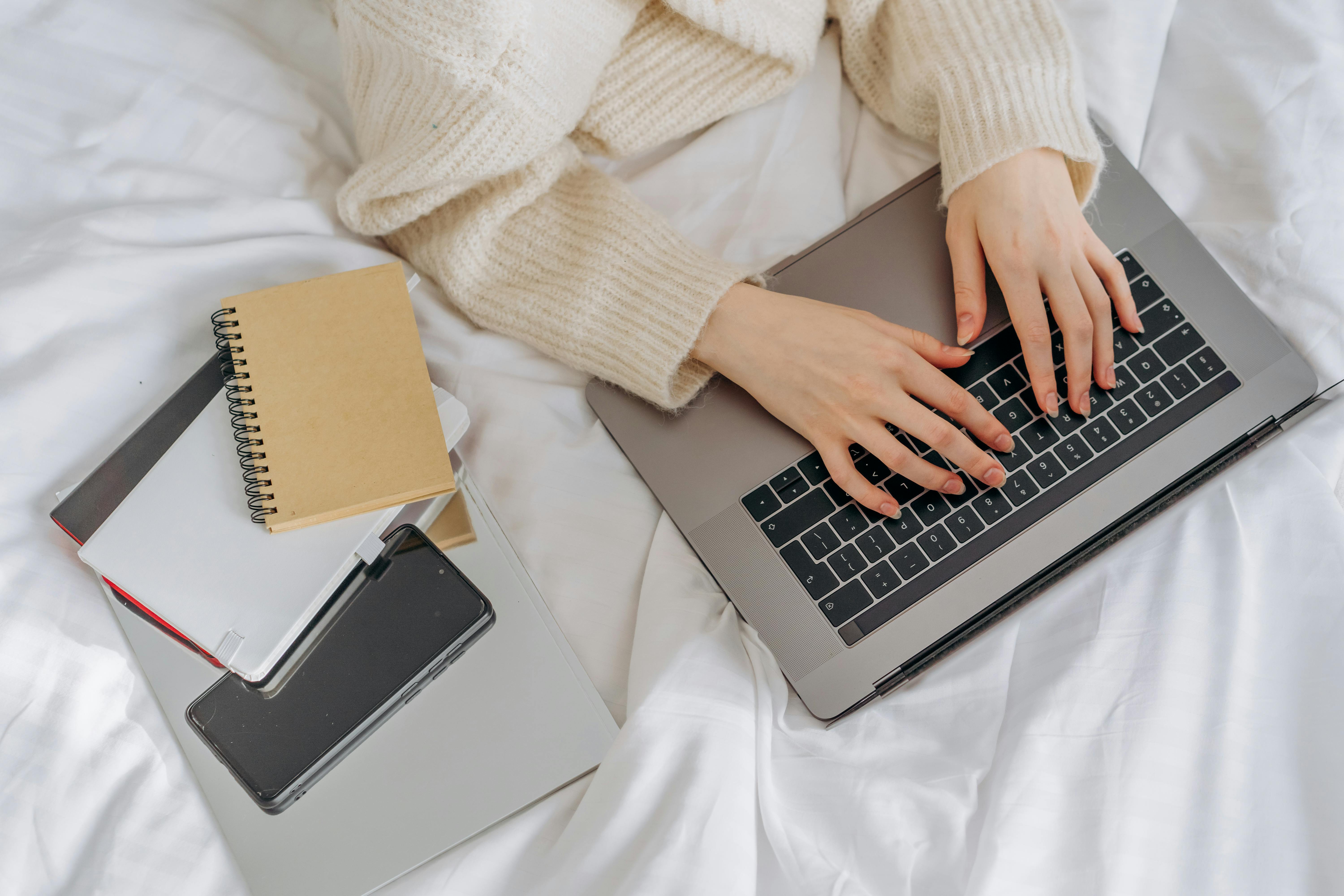 Top view of a person typing on a laptop in a comfortable setting with notebooks nearby.