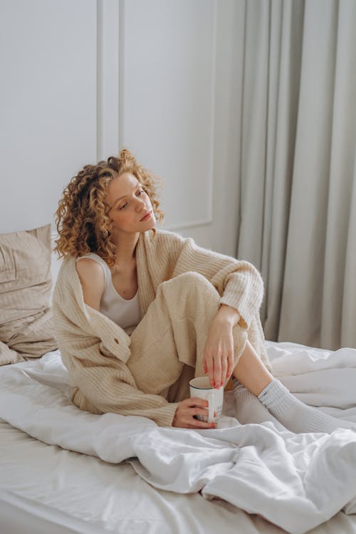 Woman in White Long Sleeve Shirt Sitting on Bed