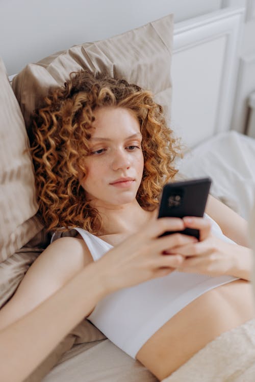 A Woman Using Her Cellphone while Lying Down on Bed