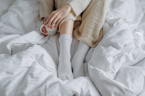 A Person Sitting on a White Blanket while Holding a Mug