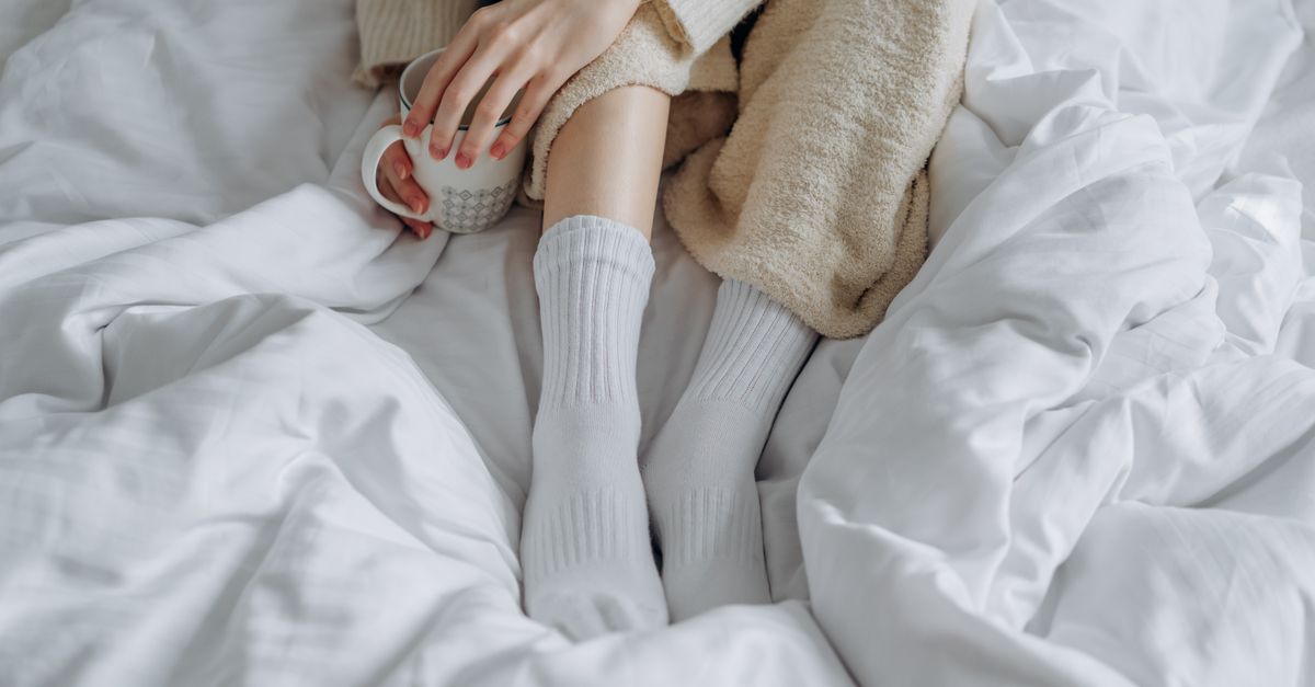 Voeten met witte sokken en handen om een warme mok op bed