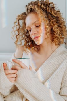 A serene woman with curly hair enjoying a cozy moment indoors, holding a mug.