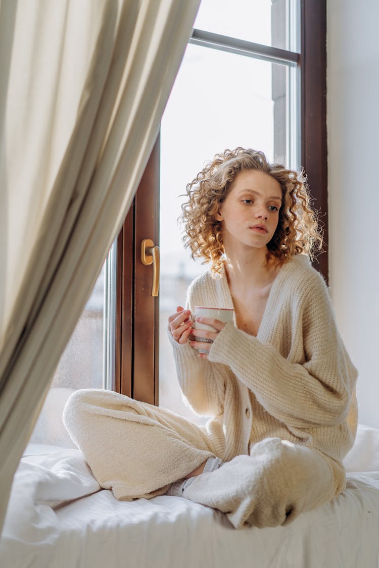 Woman In White Knit Sweater Sitting On White Linen By The Window