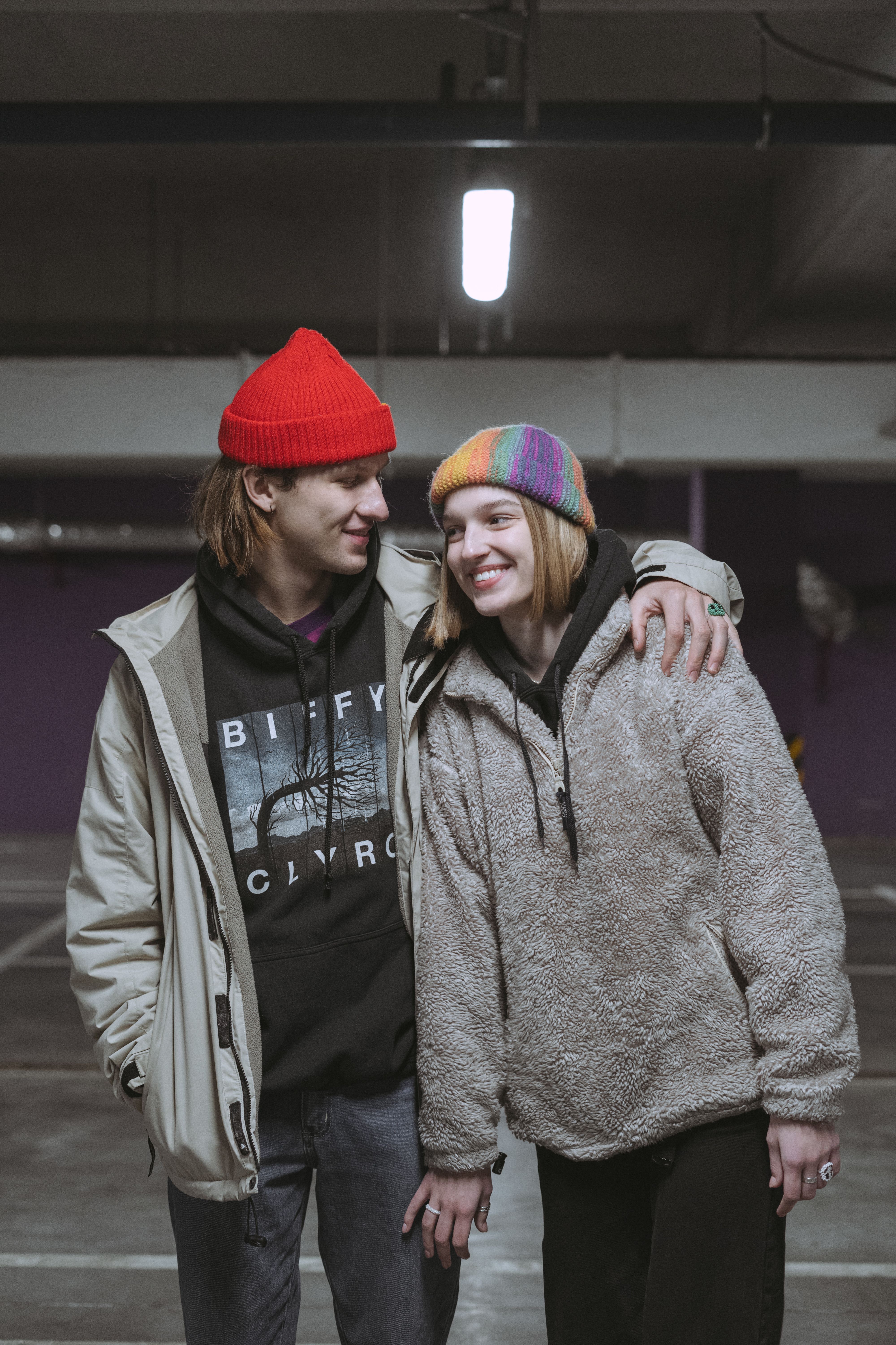 Smiling couple in casual attire sharing a side hug in an urban indoor setting.