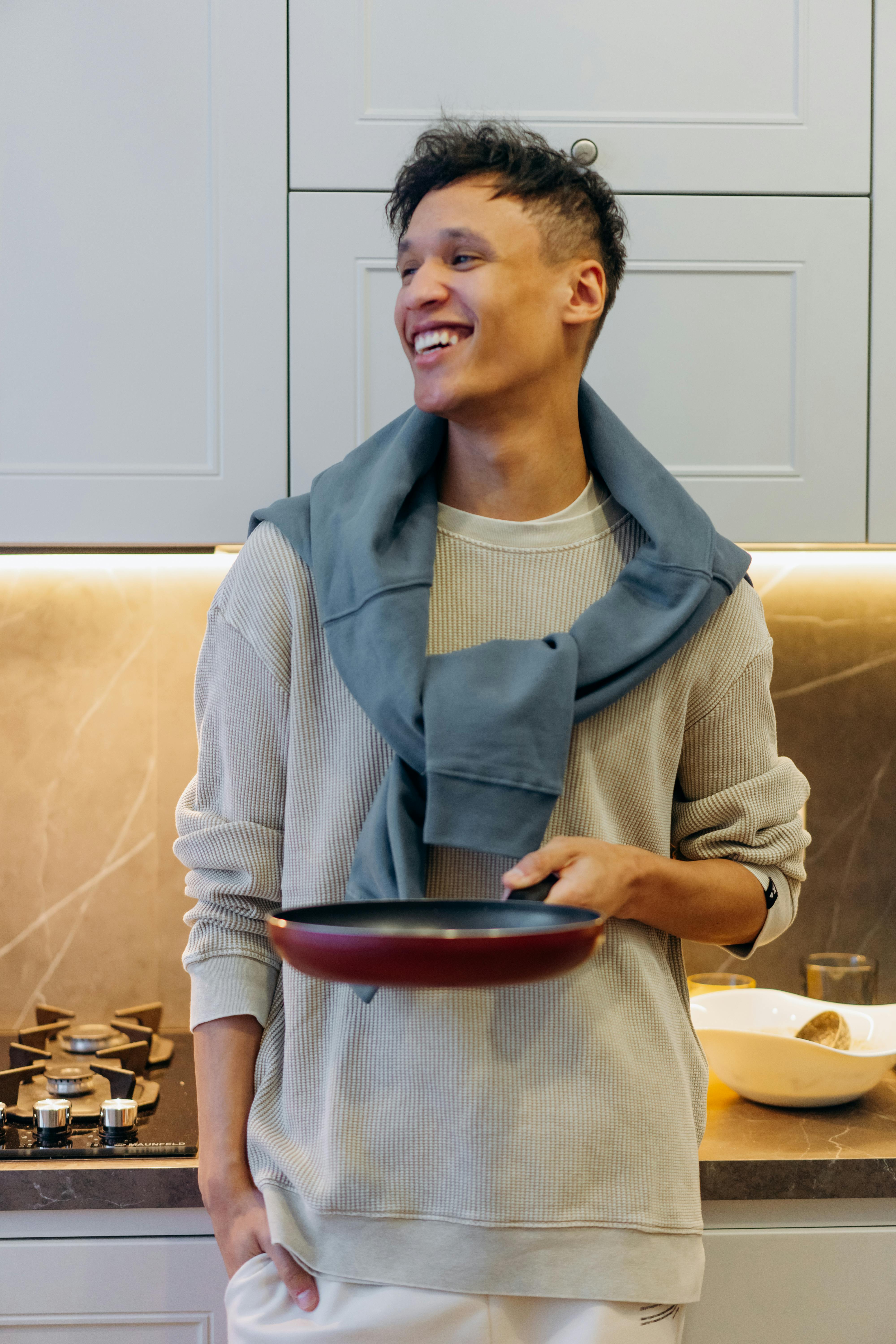 Smiling young man holding a pan in a stylish kitchen, ready to cook.
