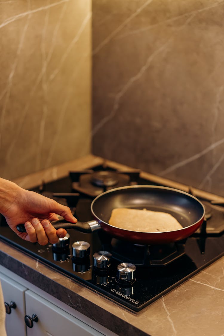 A Hand Holding A Frying Pan With Pancake On It