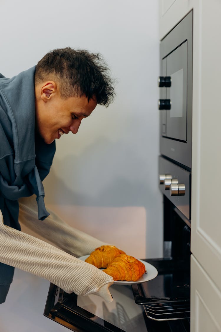 A Man Putting The Plate With Croissants In An Oven