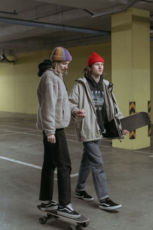 Free A young couple wearing beanies and casual clothing skateboarding indoors, holding hands. Stock Photo