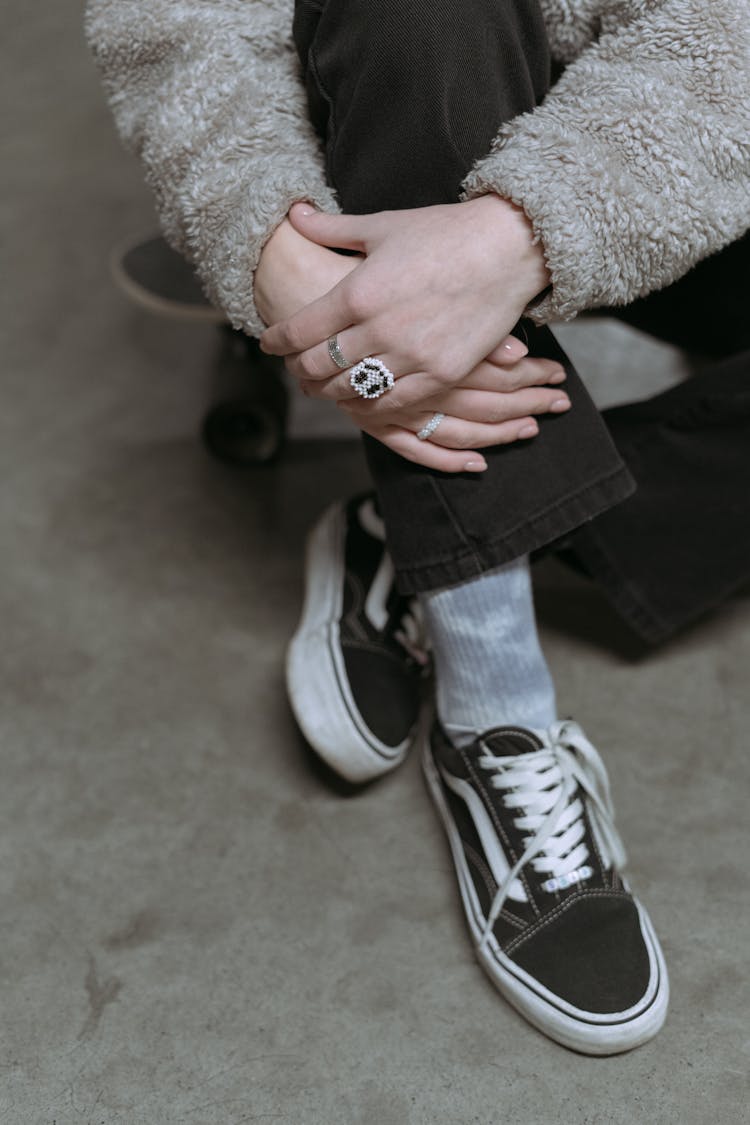 A Person Wearing Black Sneakers Sitting On A Skateboard