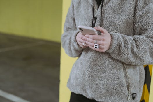 Close-up of a person texting on their smartphone with a cozy sweater in an industrial urban setting.