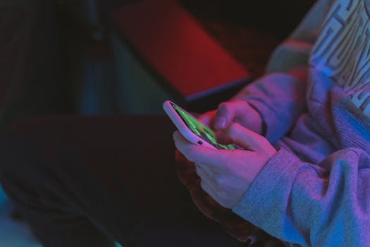 Close-up of hands holding a smartphone in a dimly lit indoor setting with neon lighting.