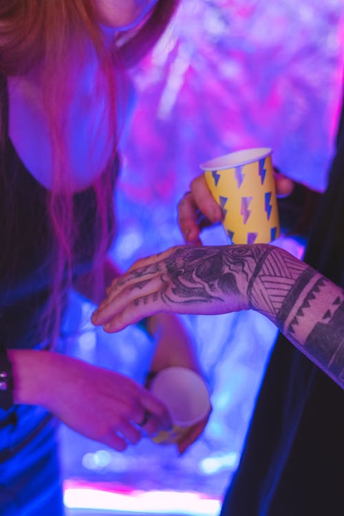 A Tattooed Person Holding Yellow and Silver Disposable Cup