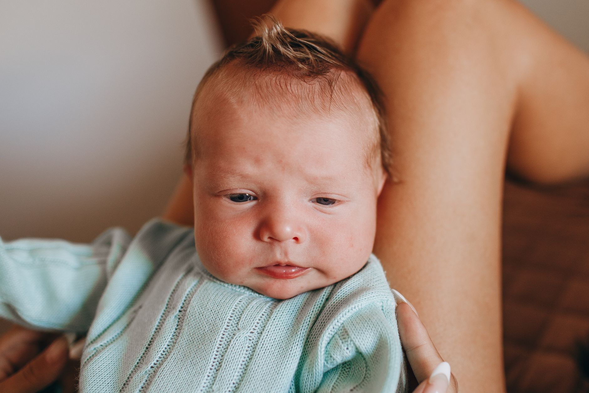 Crop unrecognizable mother with adorable little baby in wear on legs resting on comfortable bed in light bedroom at home