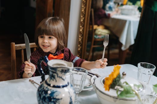 Adorable child in bow tie holding cutlery at a festive dinner table.