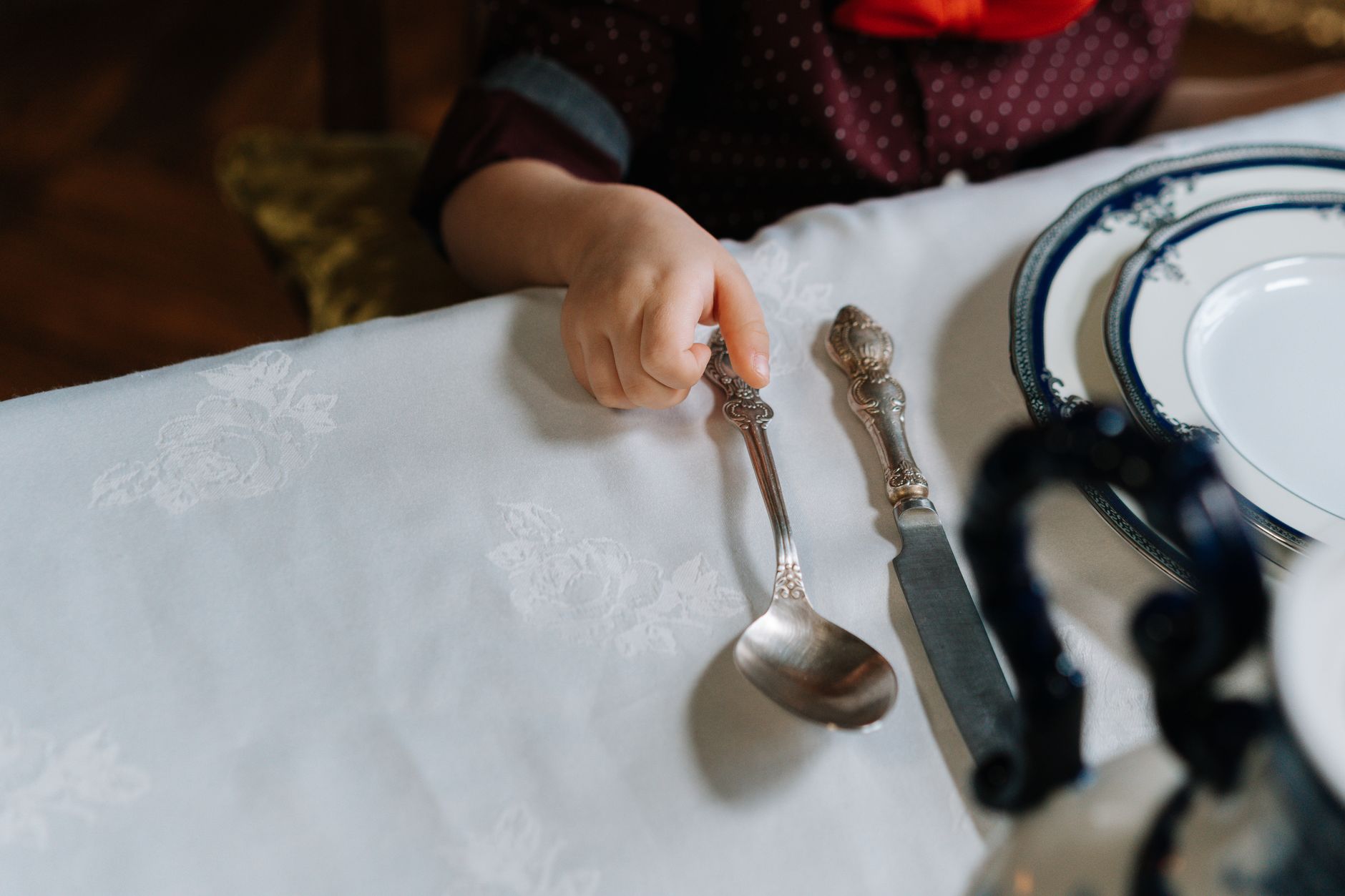 テーブルの食器に手をのばす子どもの手