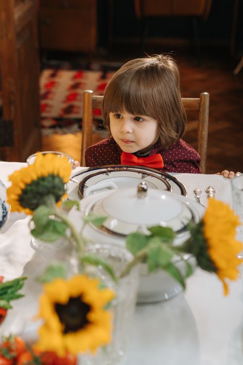 Free Adorable child at a festive table setting with sunflowers and elegant tableware indoors. Stock Photo