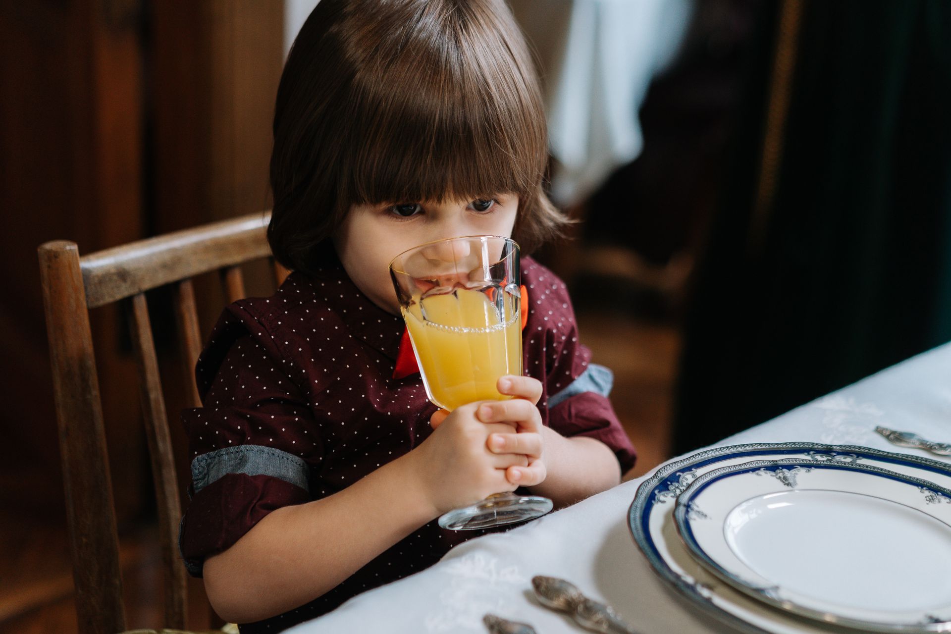 A young child drinks orange juice at a set dining table, creating a homely atmosphere.