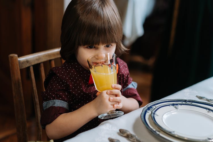 A Cute Kid Drinking A Glass Of Orange Juice