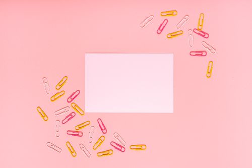 Free Flat lay of colorful paper clips with blank paper on a pink background for creative stationery concepts. Stock Photo