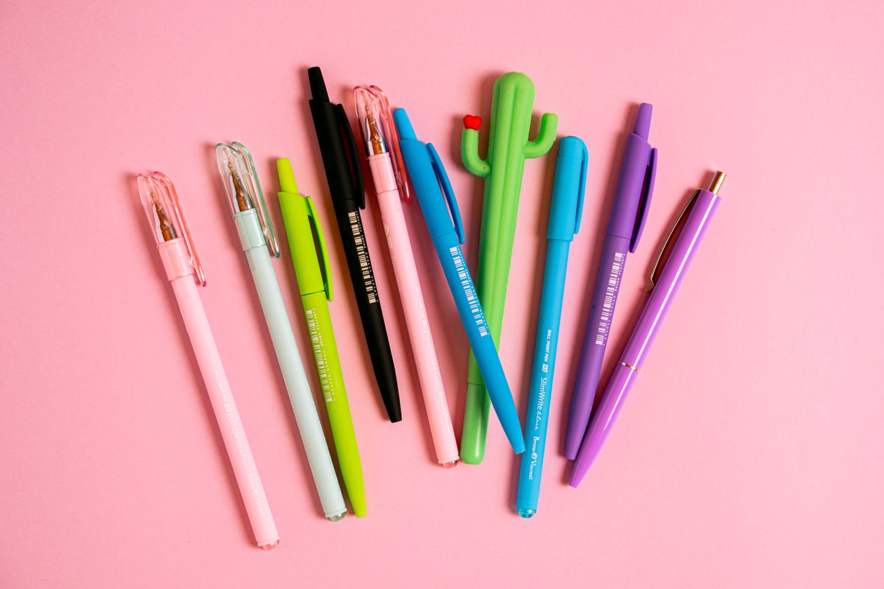 A hand holding a fountain pen with more pens visible on the desk — fountain pen collector setup